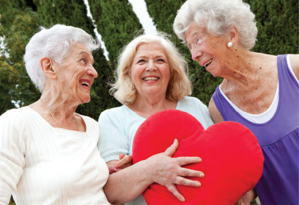 three senior women smiling while holding a red heart shaped pillow