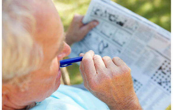 senior man doing crossword puzzle in the park