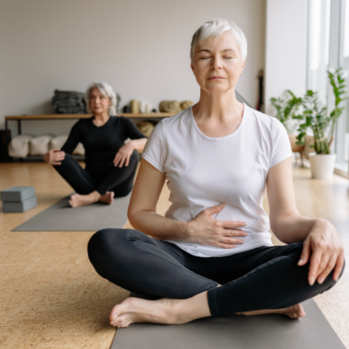 two older-adult women sitting in yoga studio meditating relaxing, calm setting