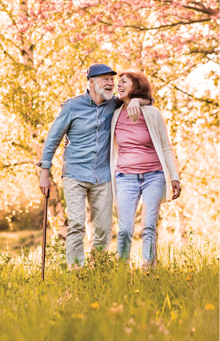 Older couple, man and woman, walking through a field of grass, in background are trees